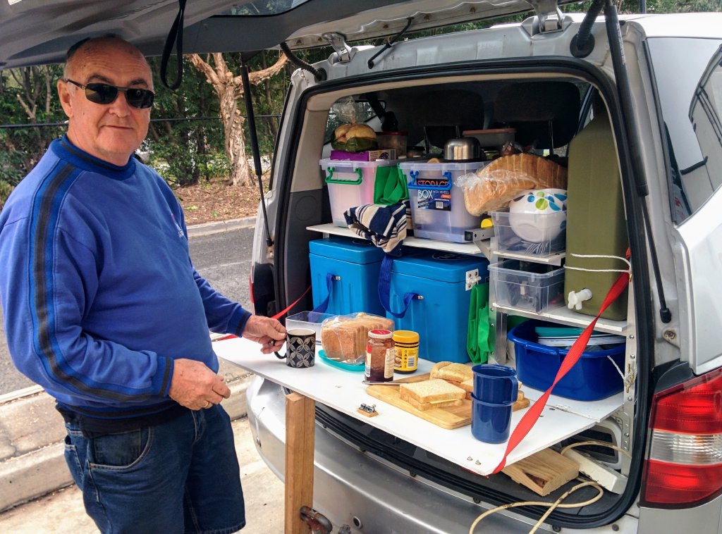 Lindsay's late father, Dennis, stands at the rear of his Ssangyong Stavic camper, boot open, making tea and sandwiches on the fold-down table.