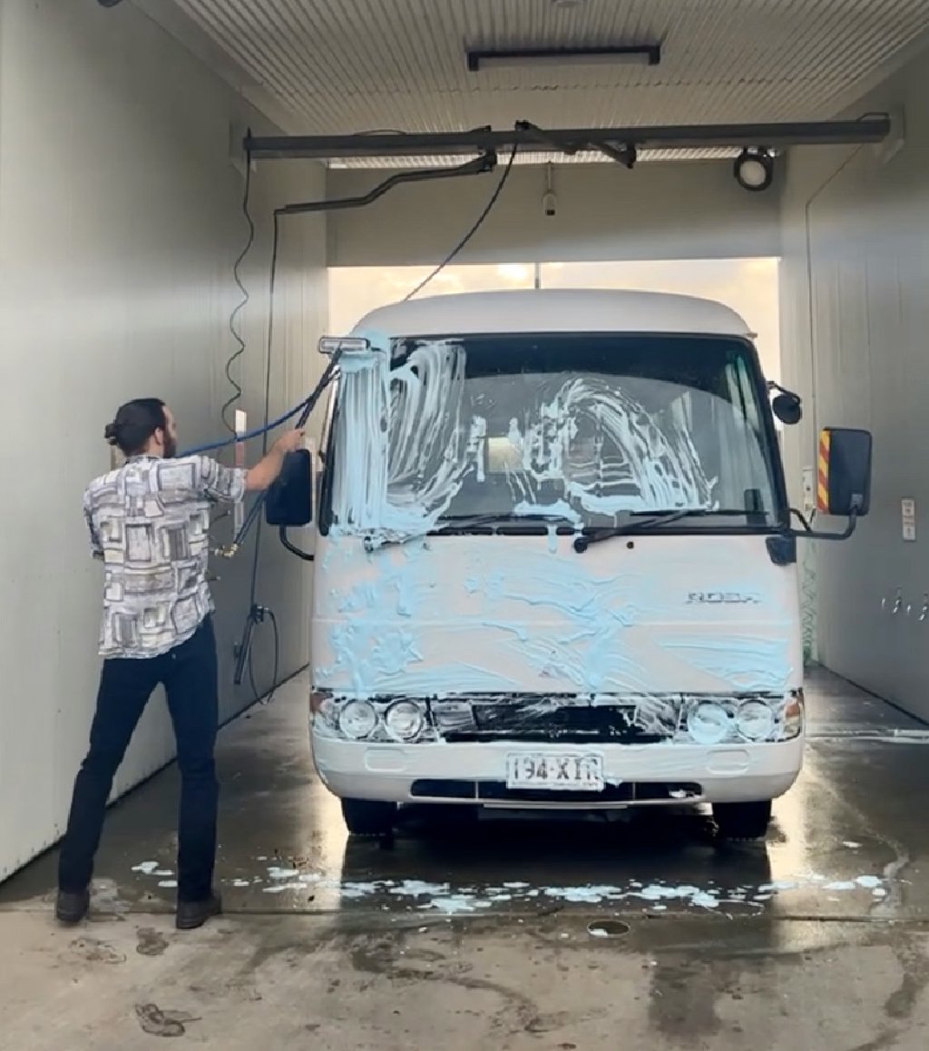 Lindsay washing the front of the bus at a manual car-wash, bus is covered in soap suds.